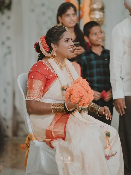 A candid shot of the bride smiling happily while seated, holding a bouquet of orange flowers.