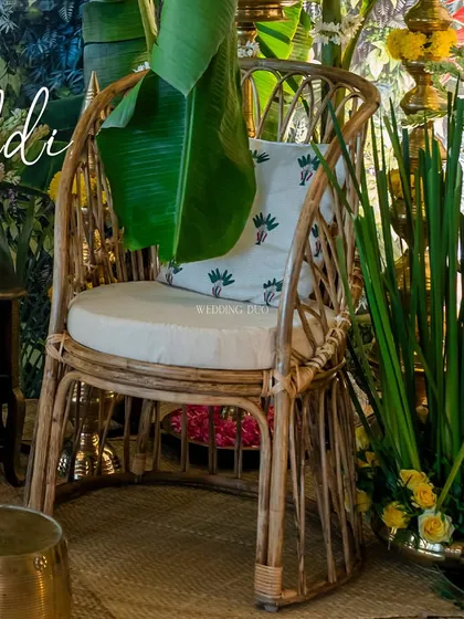 A detail of our tropical Haldi setup. A large banana leaf playfully drapes over a rattan chair, highlighting the blend of natural, woven textures and lush, green elements.