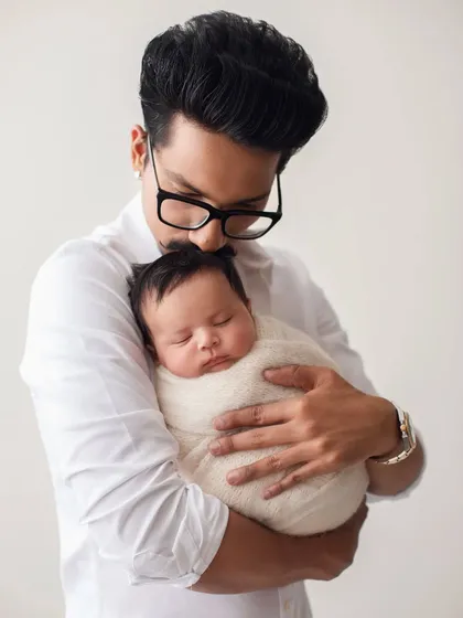 A new father, Haarsh Limbachiyaa, cradles his sleeping newborn son. A classic and timeless newborn portrait.