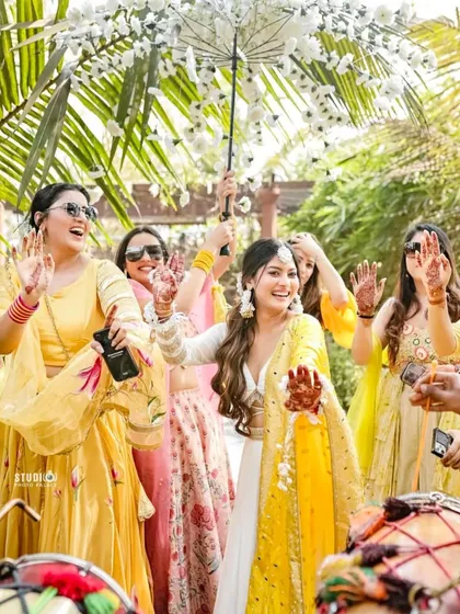The bride's entry at her Haldi, surrounded by her smiling bridesmaids. We help plan these picture-perfect moments, complete with props like this beautiful floral umbrella.