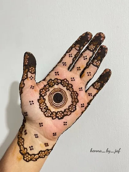 A simple and clean mandala design with a solid black center, surrounded by a ring of flowers. The fingers and wrist have matching delicate borders.