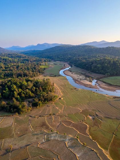 A vertical aerial shot showcasing the patterns of harvested fields next to a winding river in the Western Ghats. This perspective highlights the challenges of composing for vertical social media formats.