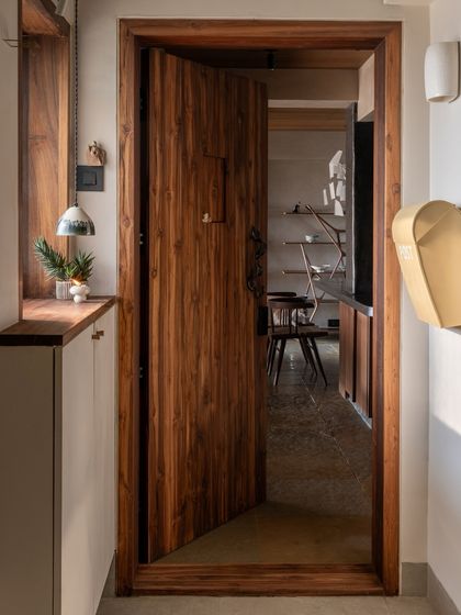 The entryway sets the tone for the entire home, with a custom teak door and a simple, functional shoe cabinet. The material palette of wood, stone, and lime-wash paint is introduced right from the entrance.
