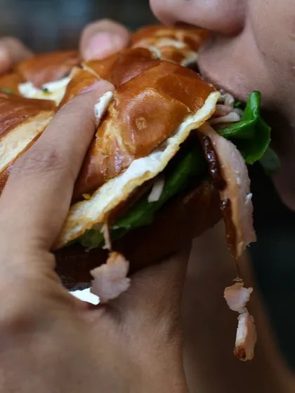 Someone taking a well-deserved, massive bite out of our pretzel bagel sandwich. It's messy in the best way possible.
