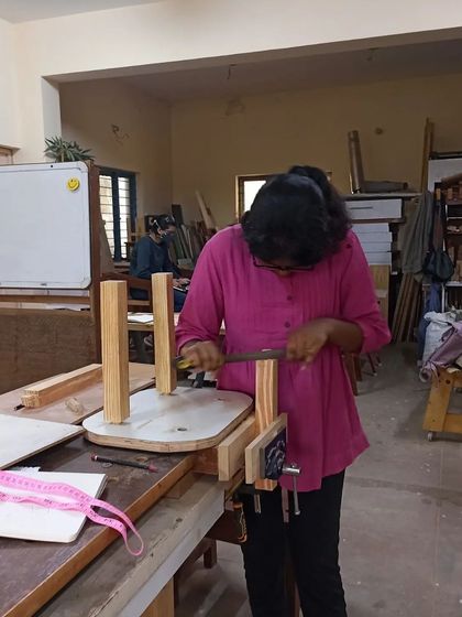 A student using a measuring tape to ensure the legs of her chair are perfectly positioned. Accuracy is key in furniture making.