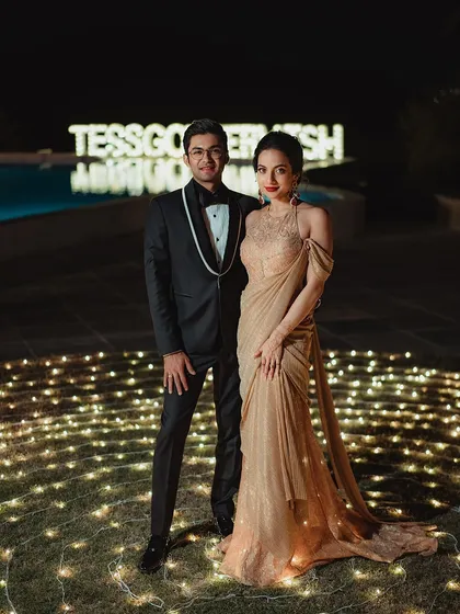 The happy couple posing against a backdrop of fairy lights. Tessa's glamorous makeup shines even from a distance, proving that a well-executed look is perfect for every photo opportunity.