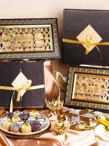 A collection of ornate, premium Diwali gift boxes filled with artisanal Indian sweets. The rich fabrics and gold accents create a sense of luxury and tradition.