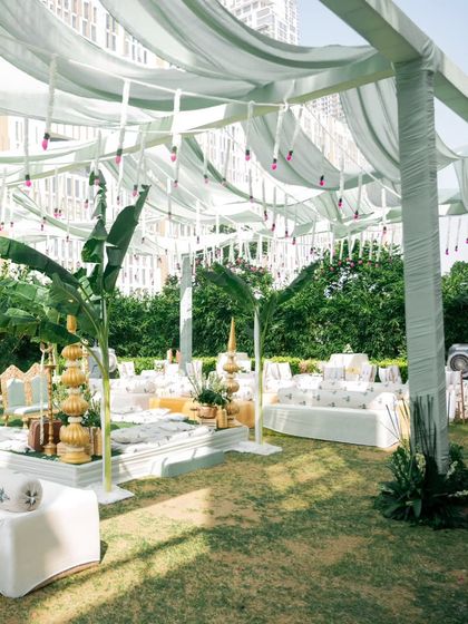 A beautiful outdoor setup for a puja ceremony, showing the seating arrangement I can coordinate. The decor features lush greenery and white drapes, creating a serene and elegant atmosphere.
