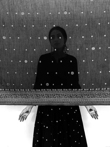 A high-contrast black and white portrait for Safaa World. The model is silhouetted behind a sheer, patterned fabric, creating a mysterious and graphic image.