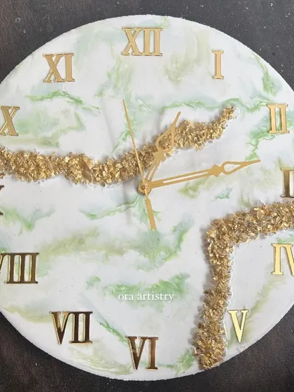 A close-up of a light green and white marble resin clock with gold crystal accents.