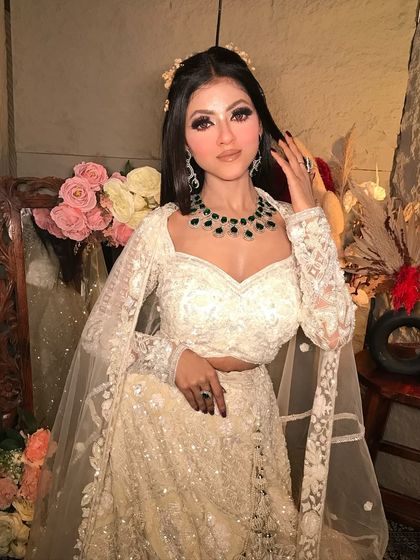 An elegant evening look in a white chikankari lehenga. The makeup is classic and glamorous, with defined eyes and a beautiful emerald necklace adding a pop of color.