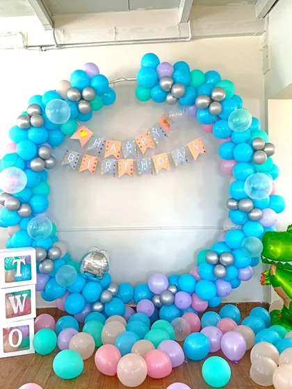 A balloon ring decoration for a second birthday. The setup uses blue and purple balloons, letter blocks spelling 'TWO', and a dinosaur foil balloon.