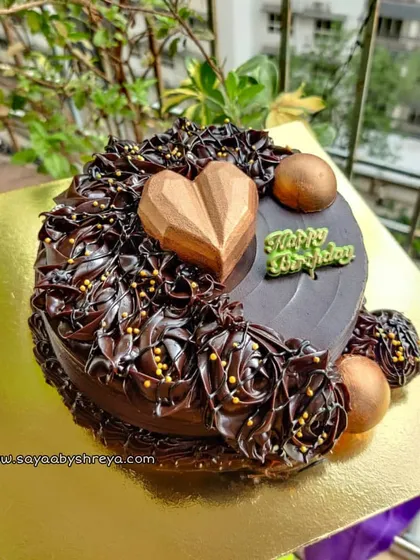 This double chocolate ganache cake is decorated with intricate piping and topped with a geometric chocolate heart and golden chocolate spheres for a modern, luxurious finish.