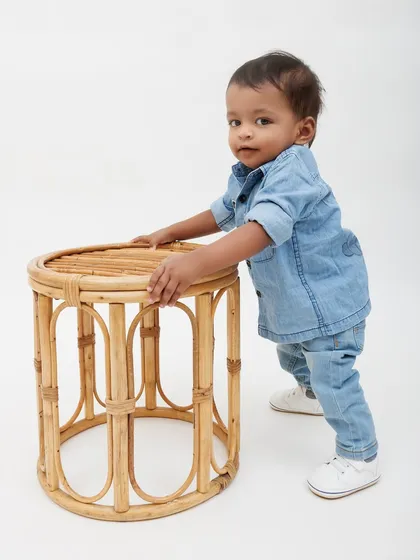 A little boy takes his first steps, holding onto a rattan stool. A perfect milestone captured during a family session.