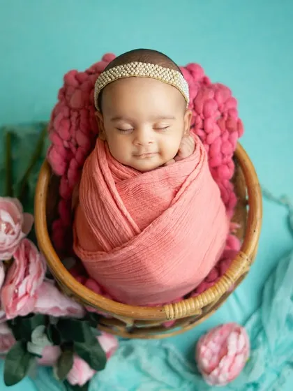 A sweet newborn girl wrapped in pink, resting in a basket surrounded by flowers. The contrast with the aqua backdrop makes the colors pop beautifully.