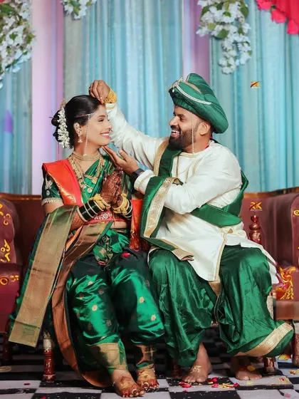 A playful and tender moment during a Maharashtrian wedding ceremony. The groom lovingly adjusts the bride's mundavalya, a candid interaction that reveals the sweet, personal connection between the couple.