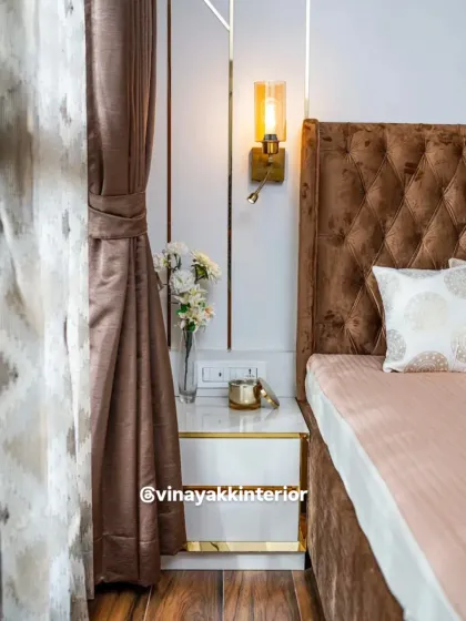 It's the small details that create a luxurious feel. This close-up shows the combination of a plush, diamond-tufted headboard, a sleek bedside table with gold accents, and an elegant wall sconce that provides warm, focused light for reading.