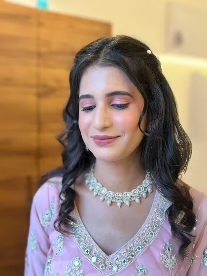 A soft and romantic look perfect for an engagement or pre-wedding shoot. The makeup features pink eyeshadow and a dewy finish, with gentle curls in the hair.