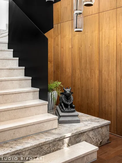 A sculpture of Nandi is placed at the base of the staircase, anchoring the space and reinforcing the home's curated, minimal aesthetic. The contrast between the black sculpture and the warm wood paneling is striking.