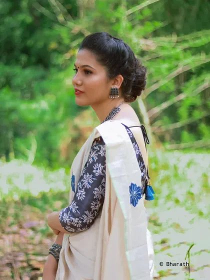 A side profile of the same off-white saree look, highlighting the model's classic bun hairstyle and the pattern on the blouse.