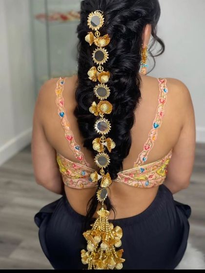 A model showing how to style a 'prandi' with mirror work and golden tassels on a long braid. This is a popular accessory for Mehendi and Sangeet functions.
