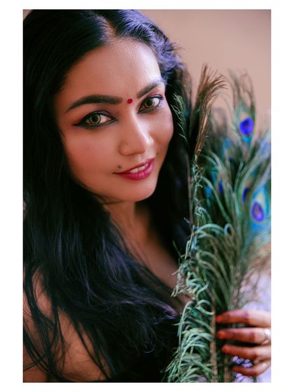 A close-up portrait of a model with a peacock feather. The image is artistic and symbolic, with a focus on beauty and nature.