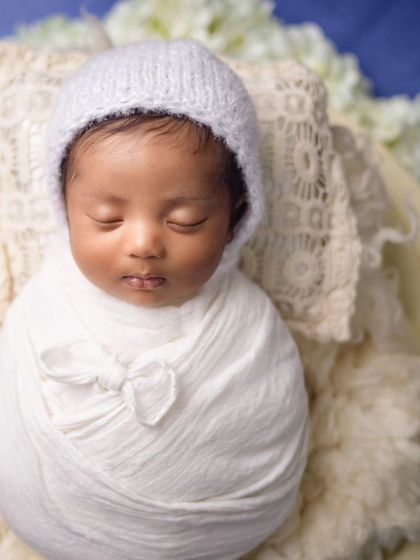 A full view of the baby in the white bonnet and wrap, showing the complete potato sack pose.