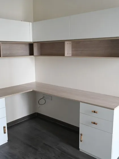 An L-shaped study workstation designed to comfortably accommodate two people. This functional desk includes ample drawer storage, overhead cabinets for books and files, and is finished in durable wood and matt laminates with elegant metallic antique handles.