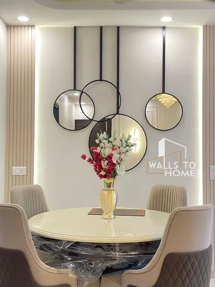 A closer look at the elegant dining setup with a round marble-top table and comfortable upholstered chairs. The decorative wall mirrors and vertical panels create a beautiful, minimalist focal point.