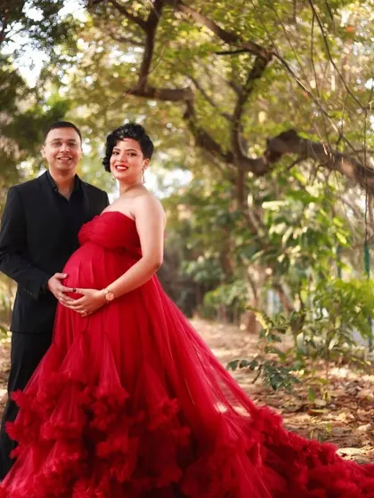 A sweet couple's portrait during their maternity session. The strapless red gown is a bold and romantic choice that perfectly complements the natural, sunlit setting.