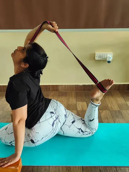 A student uses a yoga strap to work towards Poorna Rajakapotasana (Full Pigeon Pose). This is a perfect example of how we use props to safely guide the body into advanced postures.