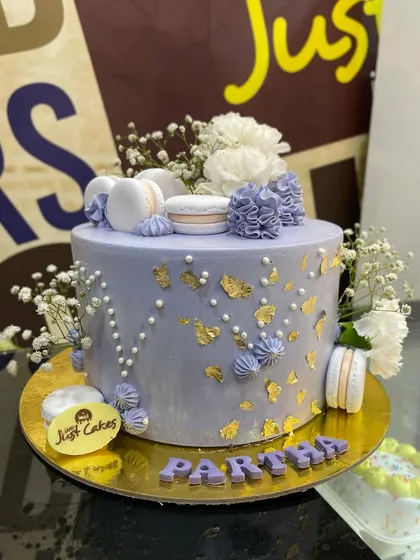 This elegant lavender cake is a beautiful example of a sophisticated design for a special occasion. It features delicate gold leaf accents, piped buttercream details, and is tastefully adorned with fresh baby's breath flowers and perfectly crafted macarons.