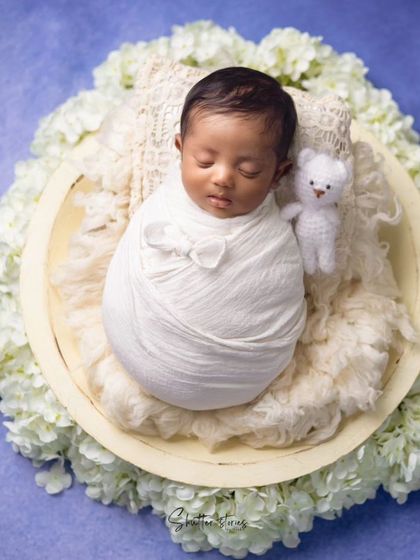 A classic bowl pose with a baby in a simple white wrap, accented with a tiny teddy bear for a touch of sweetness.