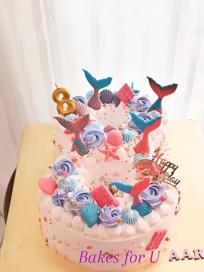 A beautiful mermaid-themed number cake, shaped into the number "8." The cake is decorated with buttercream swirls, mermaid tails, and seashells.