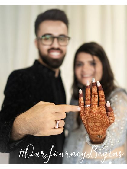 A fun and proud moment after the engagement. The couple joyfully shows off the bride's ring and intricate henna design.