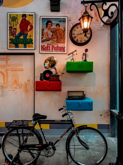 A retro-themed cafe wall in an IT office, decorated with vintage Bollywood posters, a gramophone, an old bicycle, and a classic lamppost.