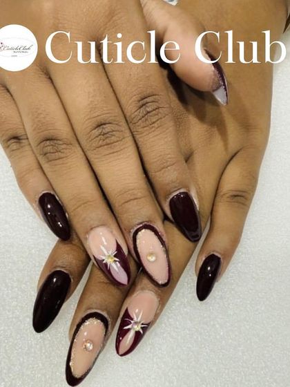 A dark and elegant design featuring deep maroon polish with negative space, accented with hand-painted stars and rhinestones.