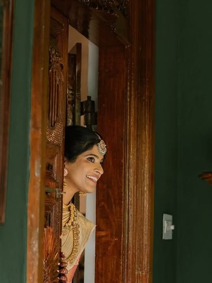 A bride peeks out from behind a wooden door, a playful and candid moment captured before the ceremony.