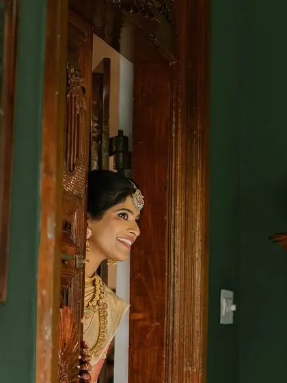 A bride, seen peeking from a doorway, her happy expression captured in the warm light of the suite.