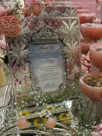 A symbol of gratitude, this pastel pink hamper is a thoughtful way to thank wedding guests. It features a silver frame with intricate palm tree motifs, dry fruit bowls, and a personalized thank you note.