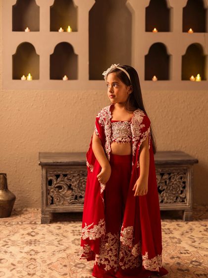 A full length view of the red cape set, showcasing the flowing cape and intricate silver embroidery.