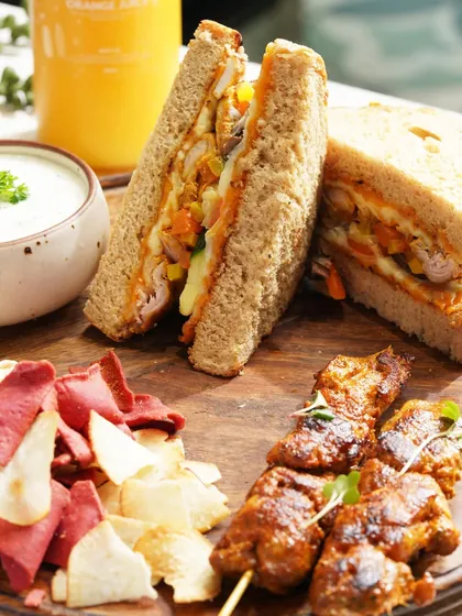 A complete meal platter featuring a hearty sandwich, chicken kebabs, and colorful vegetable chips. This shot is designed to showcase a fulfilling and delicious lunch option.