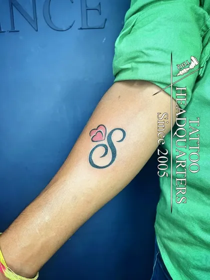 A bold initial "S" tattoo with a pink heart, a simple and popular design for showcasing a special letter.