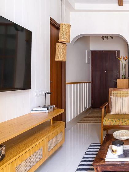 The TV unit, with its light wood and cane finish, is a perfect example of the modern farmhouse aesthetic. The striped rug and archway leading to the hallway add layers of texture and architectural interest.
