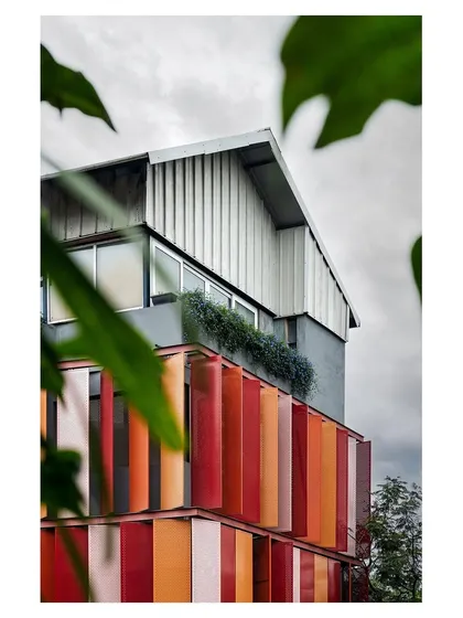 A view of the building with the red kinetic facade, framed by foliage. The design shows how a contemporary, industrial building can coexist with nature.