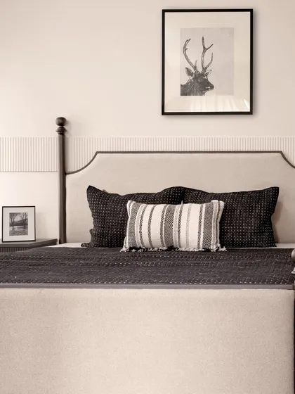 The half-poster bed in the master bedroom is adorned with plush, muted-tone cushions, creating a restful and inviting focal point. The framed art above the bed adds a personal touch.