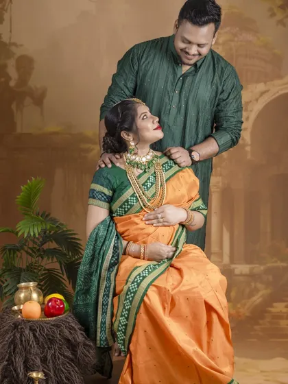 A loving couple's portrait in traditional Odia attire. The mom-to-be is radiant in an orange and green saree, her look completed with beautiful gold jewelry.