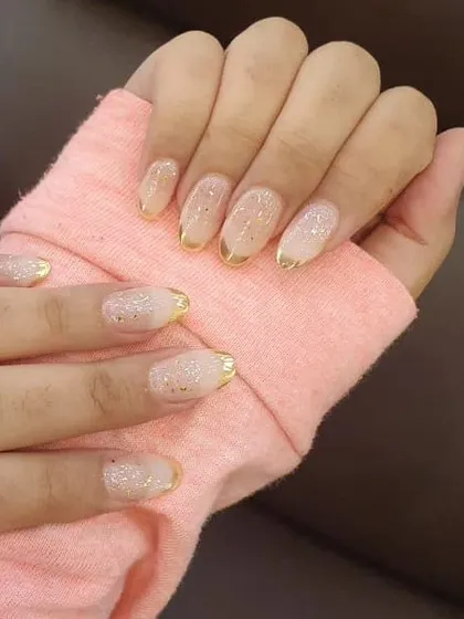 A beautiful set of gel extensions with a subtle glitter base and a delicate gold chrome French tip for a touch of luxury.