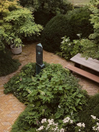 An overhead view of a secluded garden seating area. A simple wooden picnic table and bench are surrounded by dense foliage, creating a private dining spot that feels completely immersed in nature.