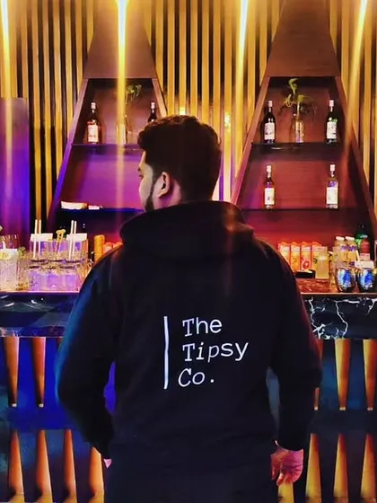 A team member proudly wearing The Tipsy Co. jacket, looking over a beautifully lit bar. This shot represents our brand identity and the world of experiences we create.